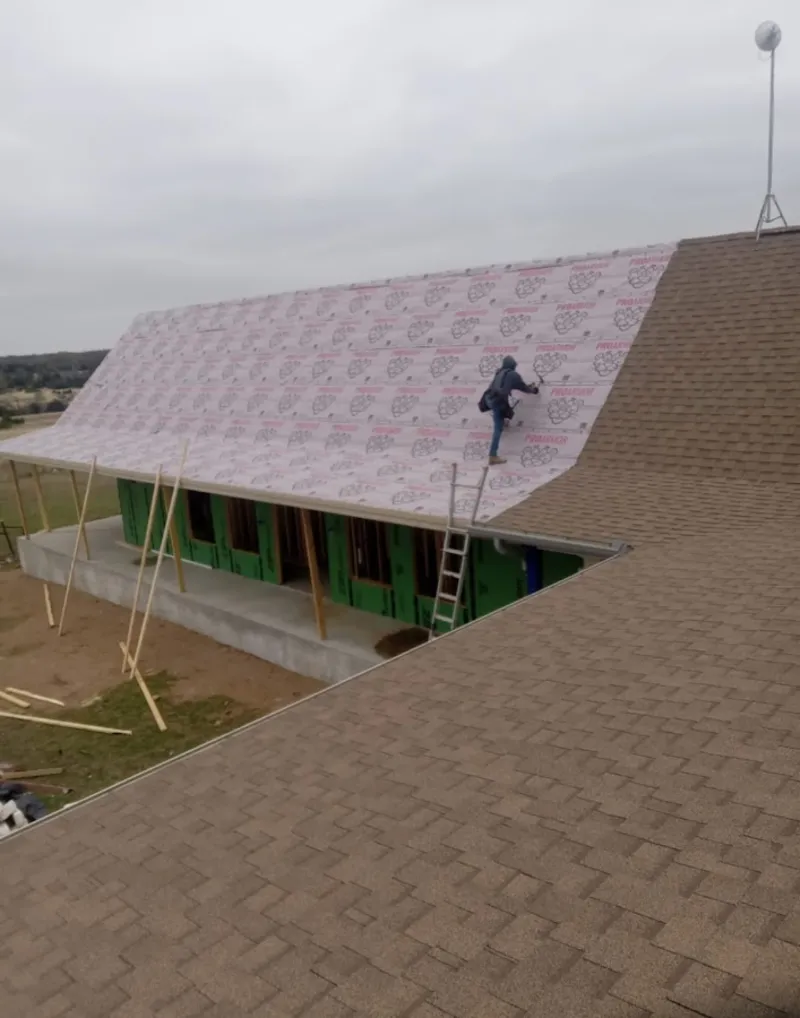 Worker preparing underlayment for a metal roof installation in Harvey